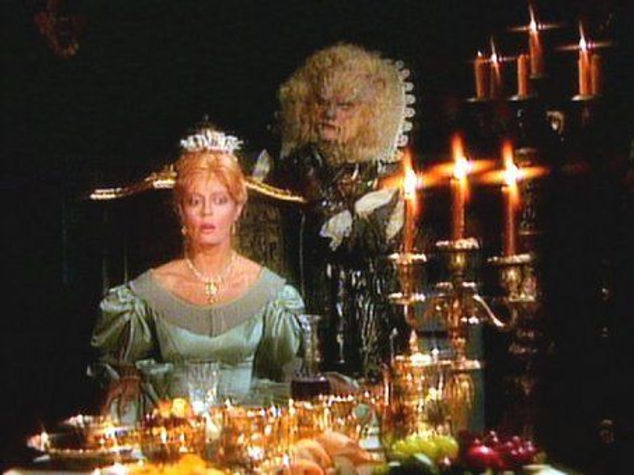 Beauty sits at an elaborate dinner table with The Beast behind her